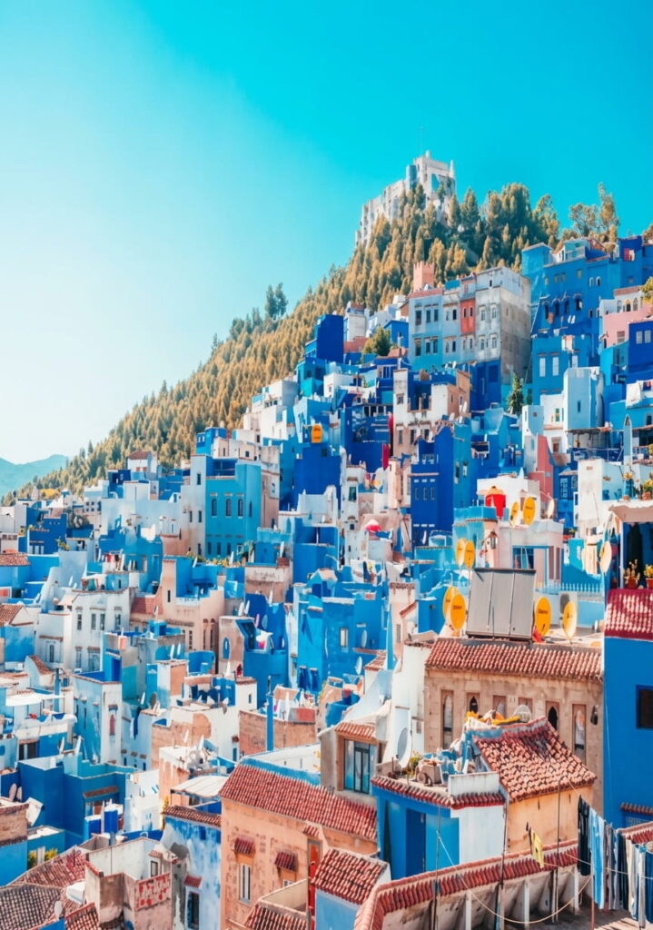 Vibrant blue buildings cascade down a hillside in Chefchaouen, Morocco, showcasing the town's unique architecture against a clear blue sky.